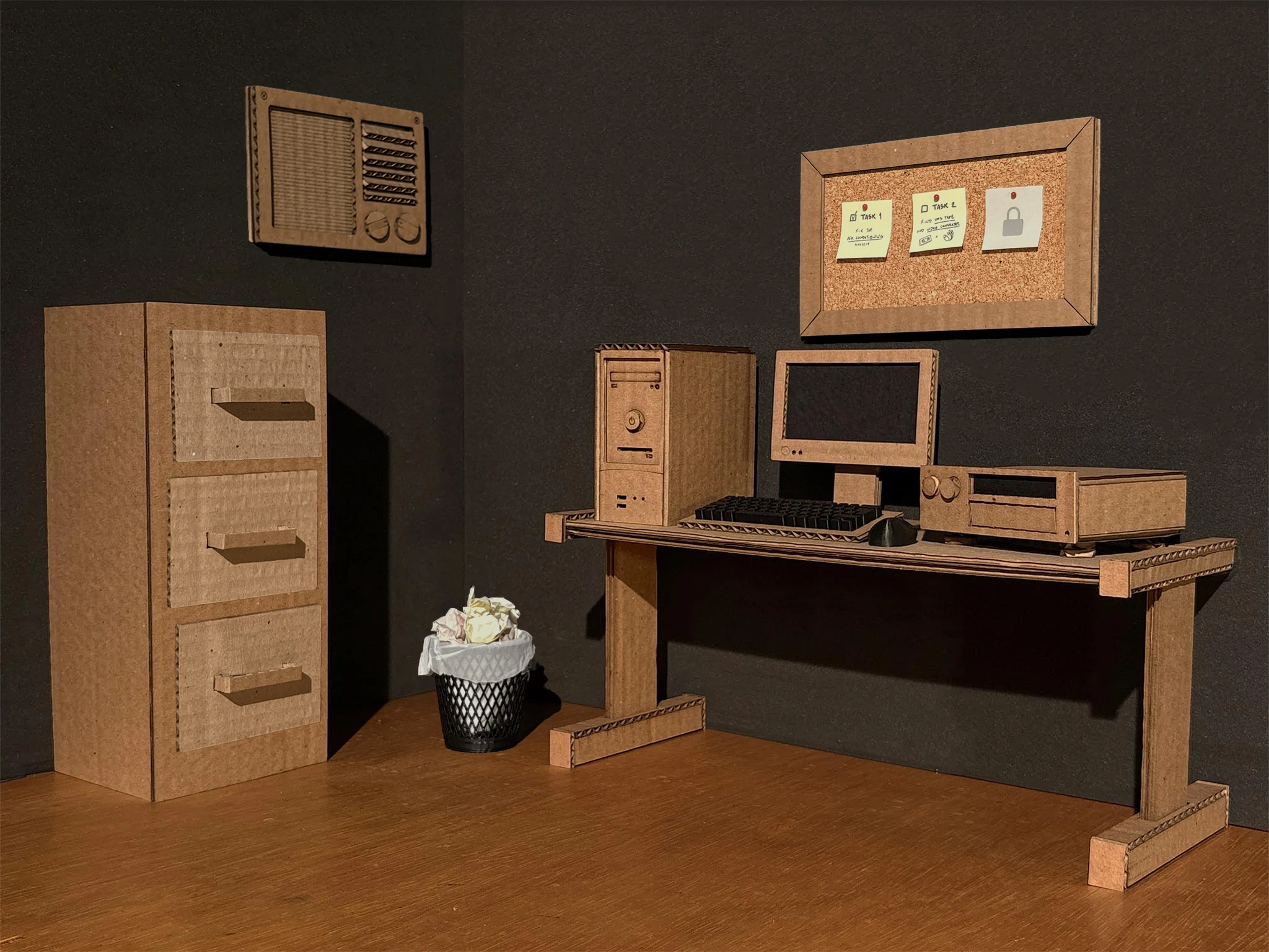 The archive room from MIS Archive: a filing cabinet, a desk with a computer and a VHS deck, a bin and a task board, all built in cardboard.